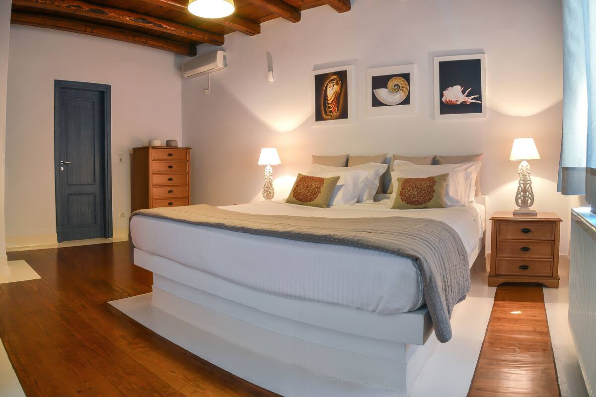 A bedroom with a large bed, wooden nightstands, and wall-mounted lamps.