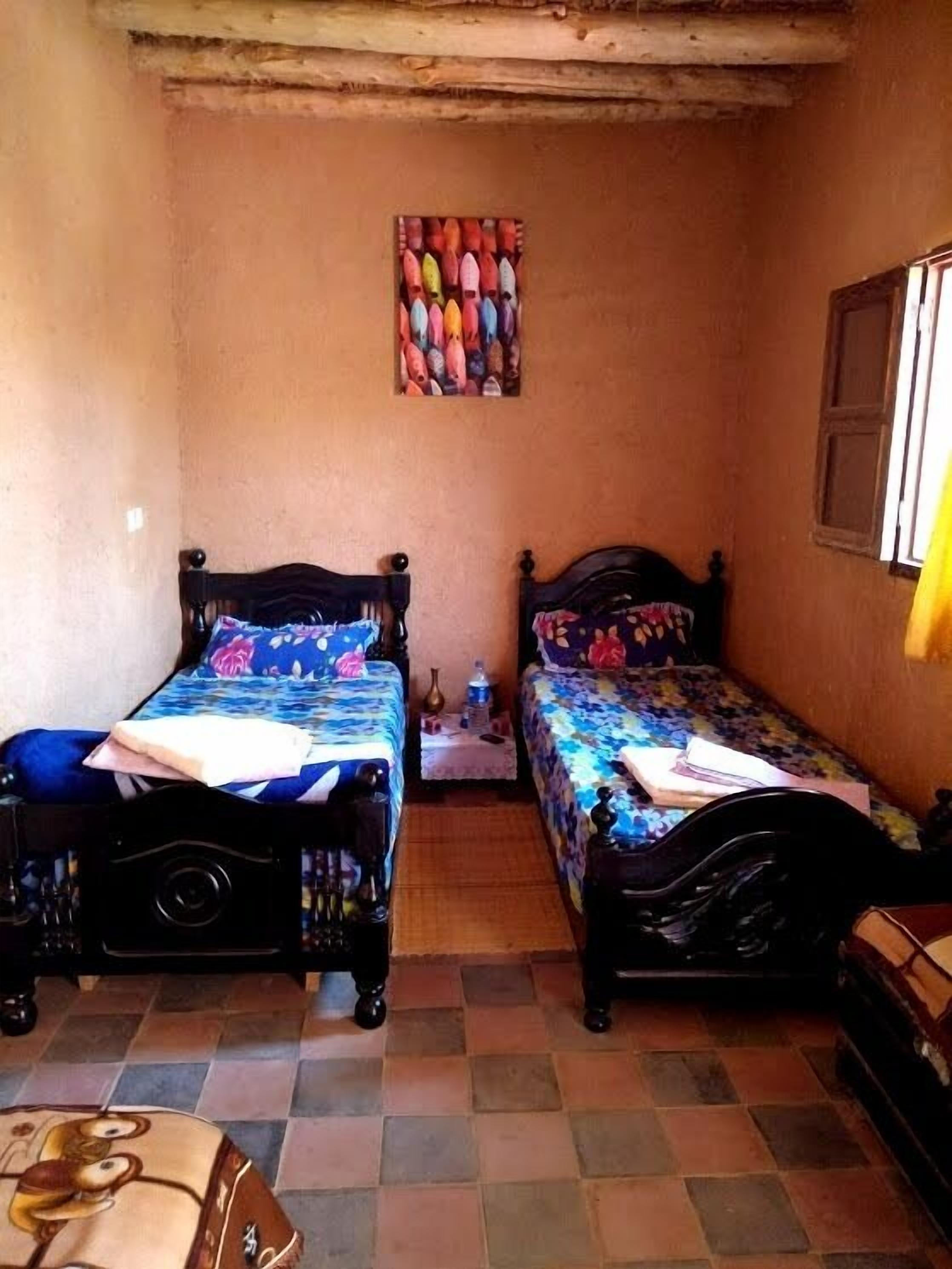 A small, cozy room with two wooden beds, a tiled floor, and a wall-mounted shelf with colorful objects.