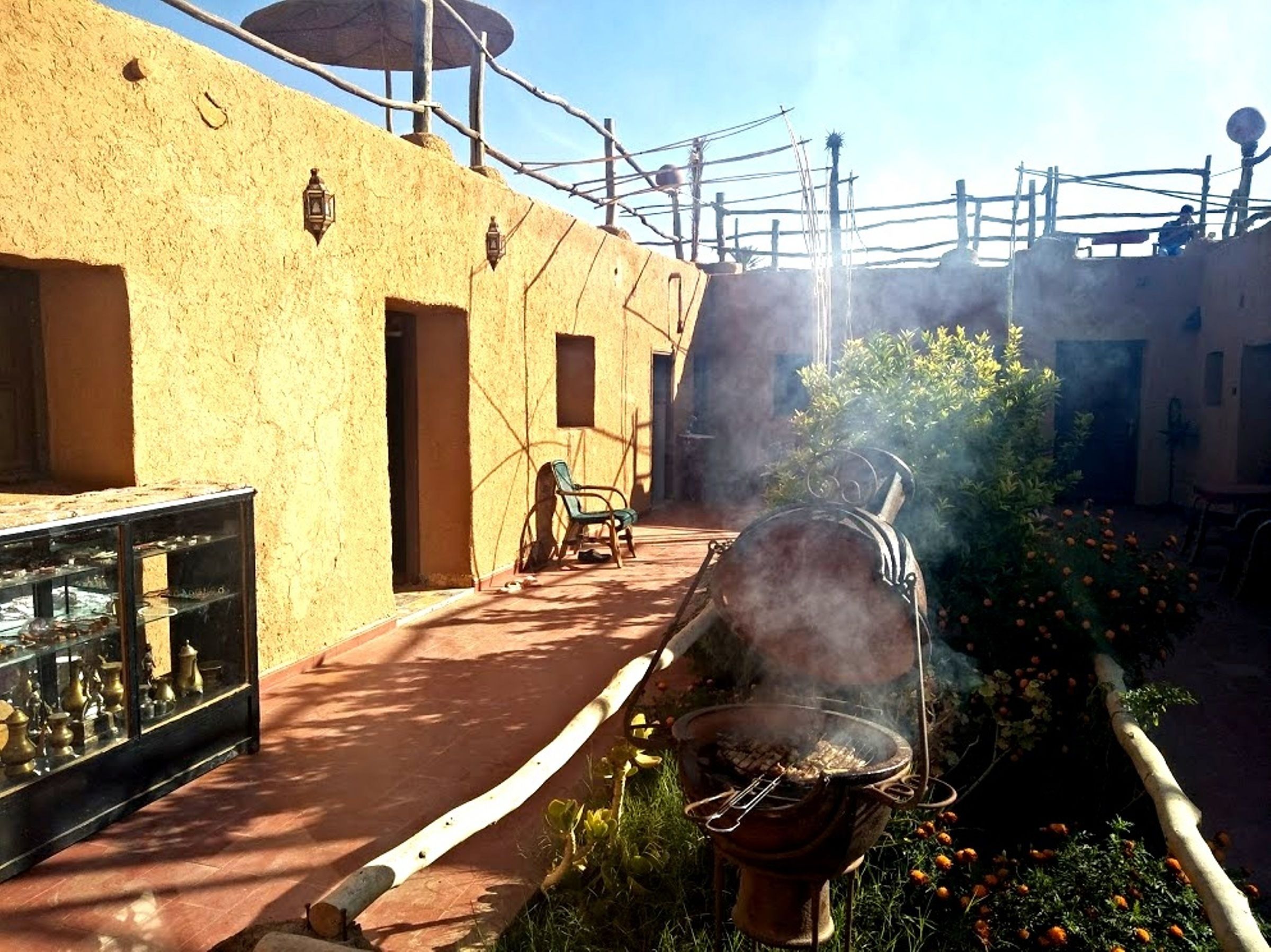 Un patio con una parrilla exterior tradicional, una vitrina de vidrio con objetos y un edificio de fachada texturizada.