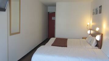 A hotel room with a bed, bedside table, wall-mounted lights, and a door leading to another room.