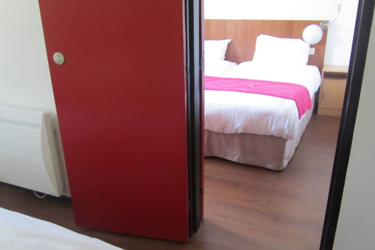 Una habitación de hotel con una cama, una puerta roja y suelo de madera.
