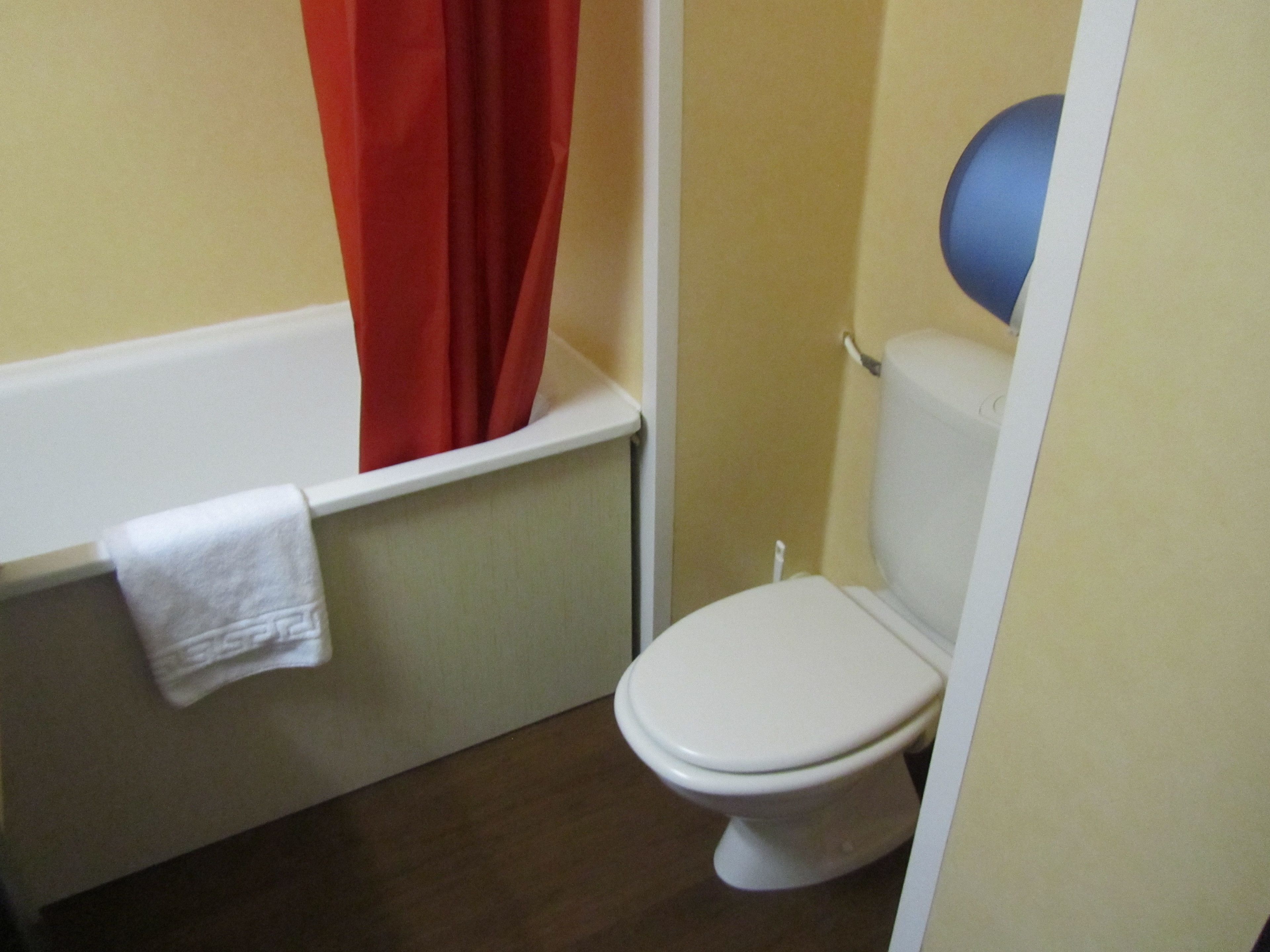 Un baño pequeño con un inodoro blanco, una cortina de ducha roja y una toalla blanca colgada en la pared.
