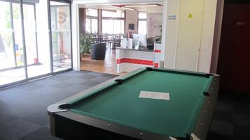 A pool table in a room with a glass door leading to an outdoor area with tables and chairs.