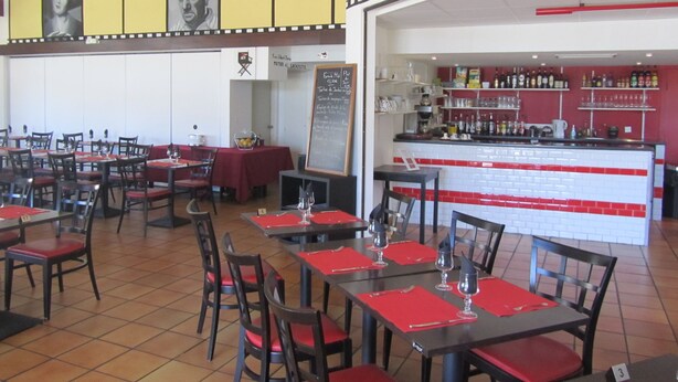 A restaurant with multiple tables and chairs, a bar area with shelves of bottles, and a chalkboard menu. - Hôtel Le Saint-Joseph (Saint-Éloy-les-Mines)