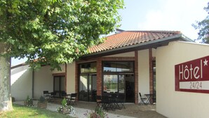 A hotel with a patio area, outdoor seating, and a sign indicating 24/24 availability. - Hôtel Le Saint-Joseph (Saint-Éloy-les-Mines)