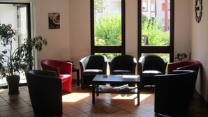 A room with a red sofa, black armchairs, and a coffee table. There are large windows with a view of greenery outside. - Hôtel Le Saint-Joseph (Saint-Éloy-les-Mines)