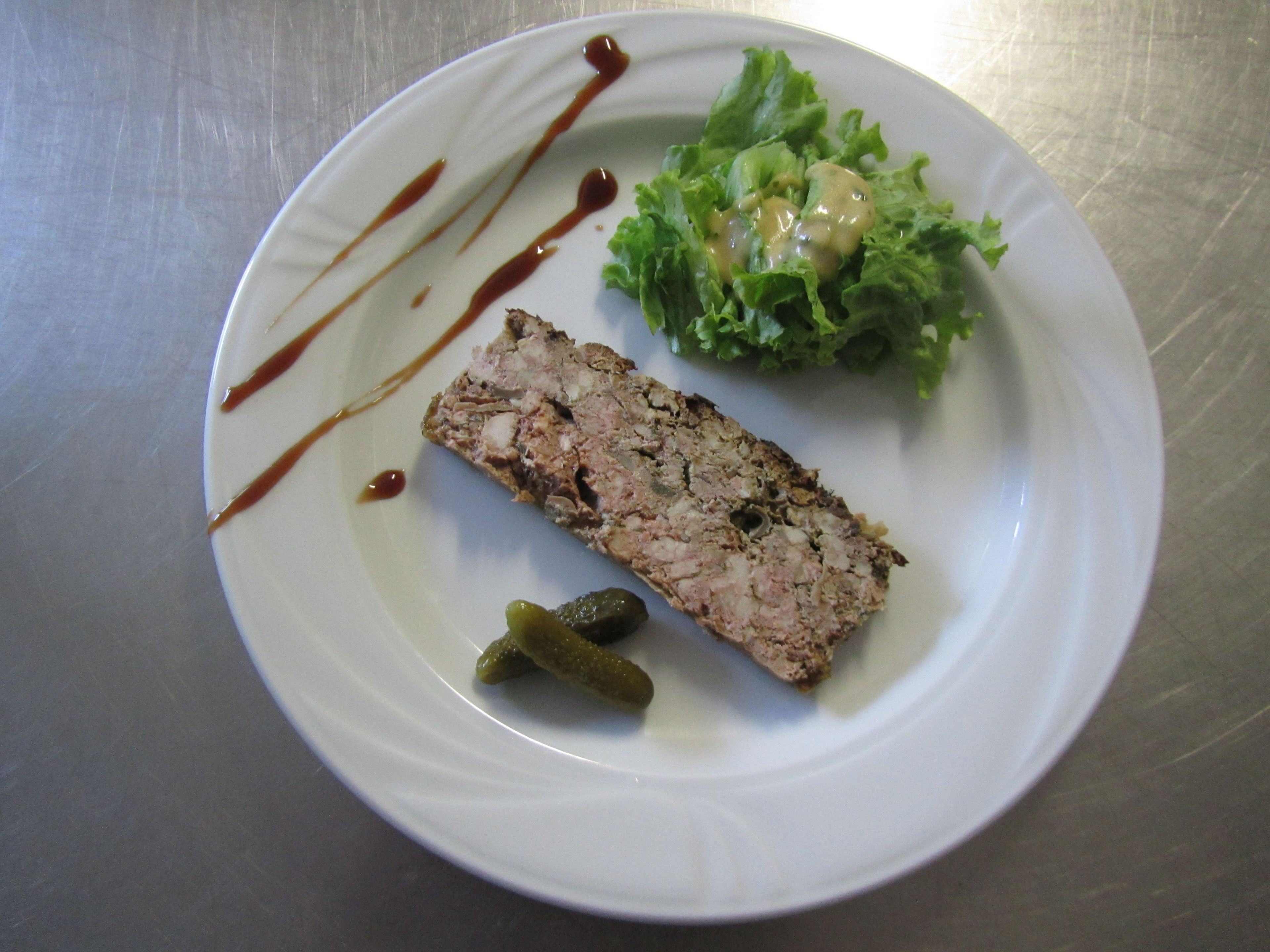 Une assiette blanche avec une tranche de viande, une portion de laitue et un cornichon.