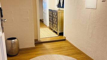 A hallway with a round beige rug, wooden flooring, a white door, a decorative wall piece, and a small potted plant.