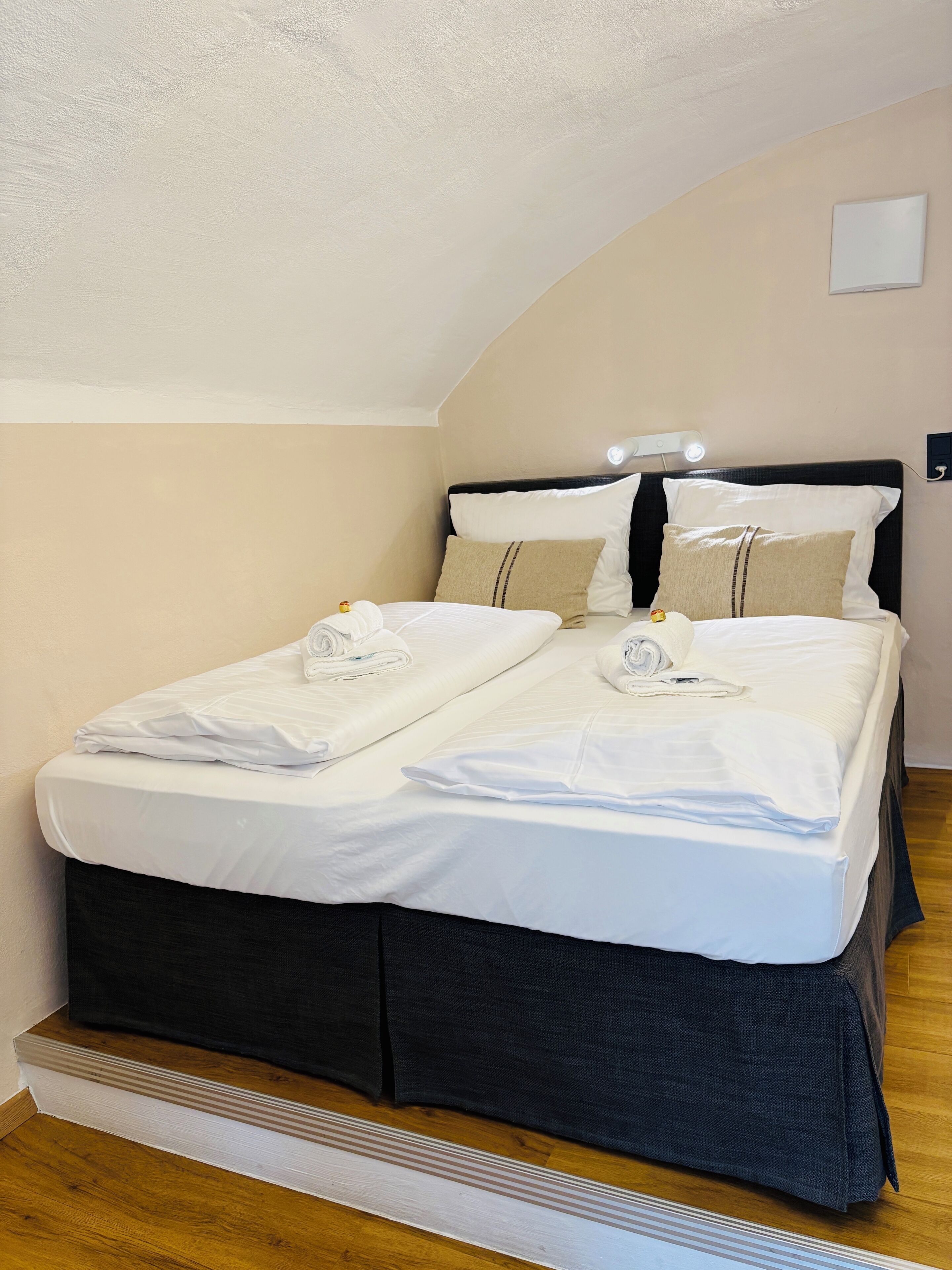 A neatly made double bed with white linens, a dark headboard, and a bedside lamp.