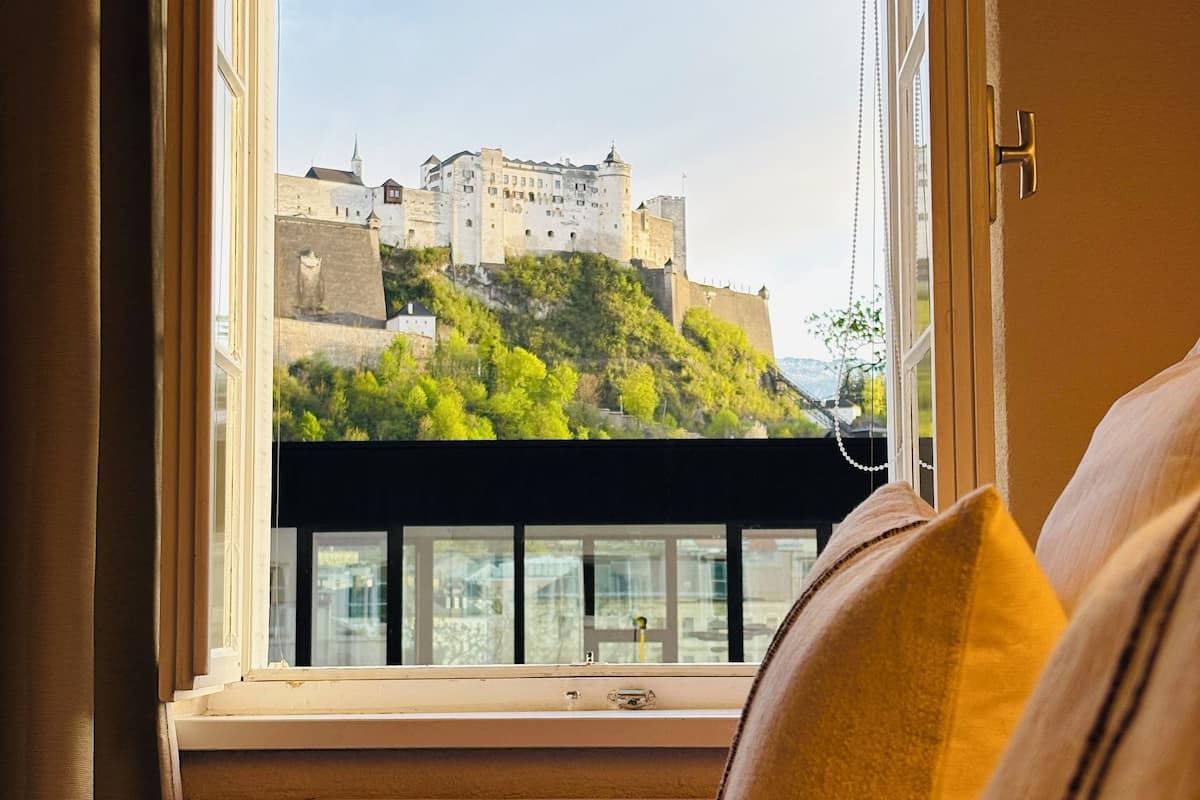 A hotel room with a large window offering a view of a castle on a hill.