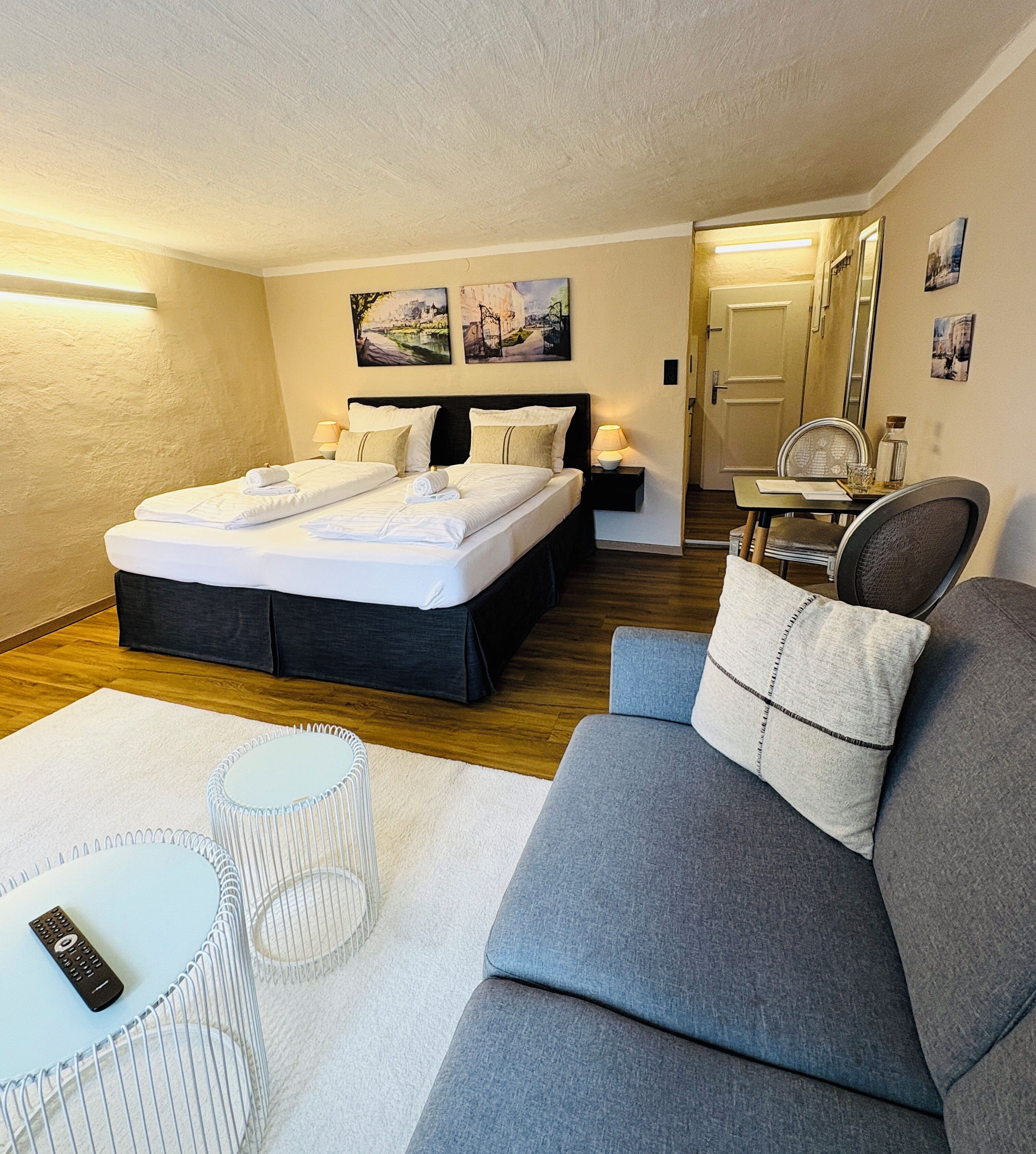 Ett hotellrum med en stor säng, en grå soffa, ett litet bord och en stol.