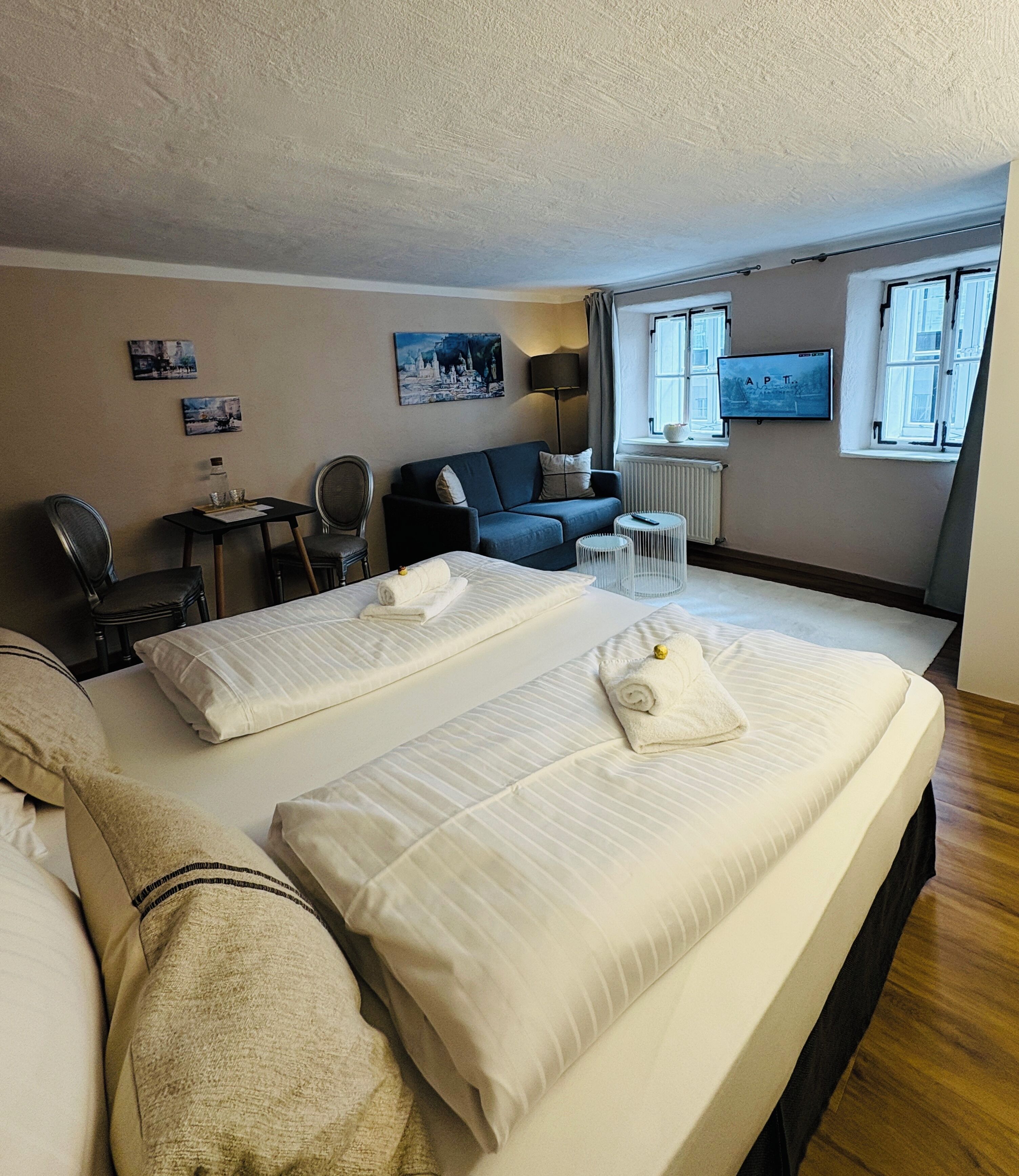 A hotel room with two beds, a desk, a chair, a TV, and a window.