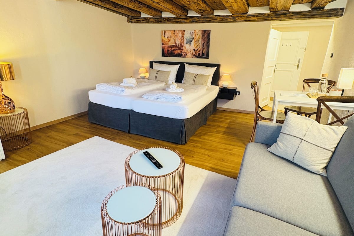 A bedroom with a large bed, two bedside tables, a sofa, and a wooden ceiling.