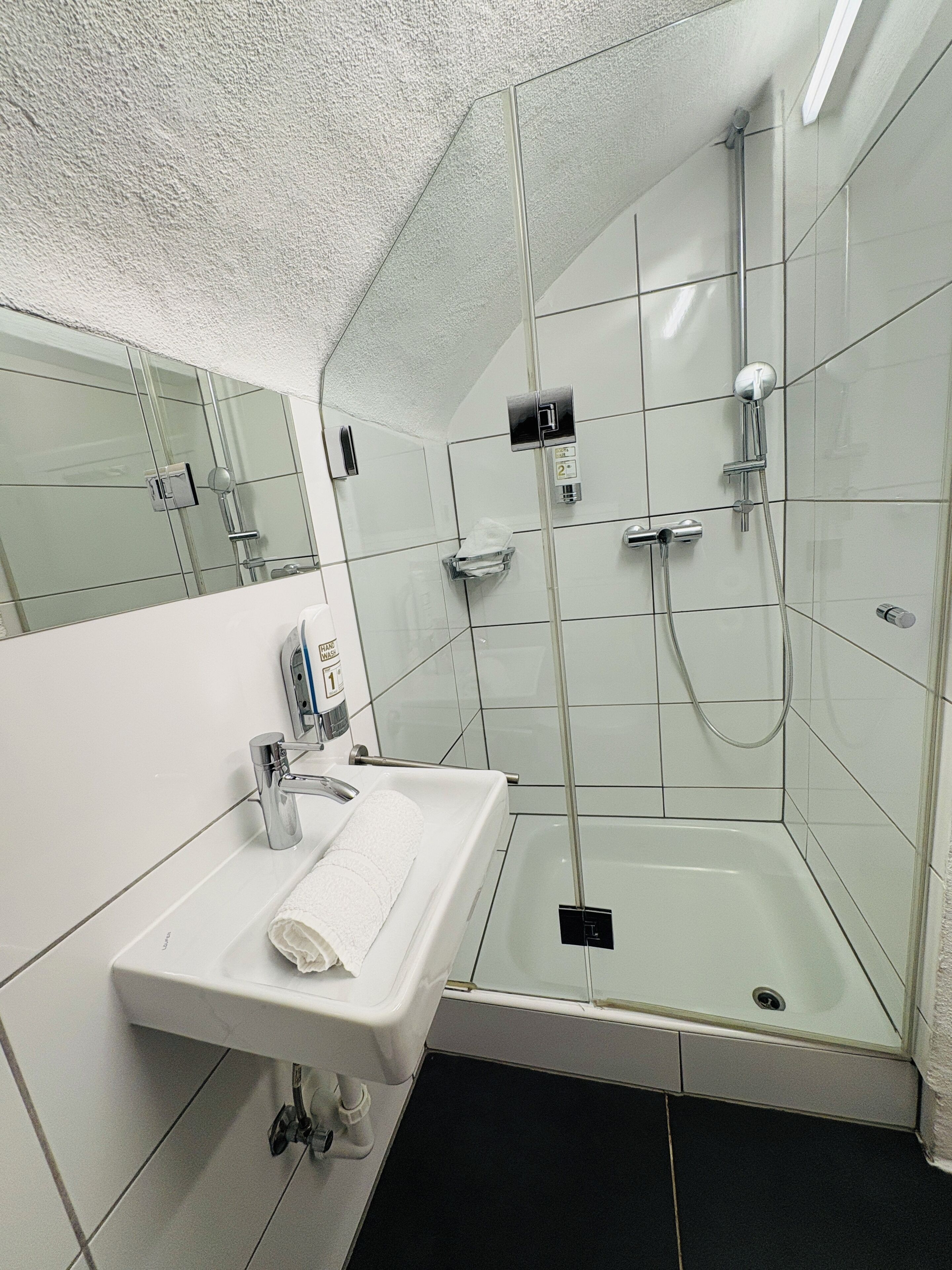 Een moderne badkamer met een douchecabine van glas, een wit wastafelmeubel met een handdoek en een spiegel.