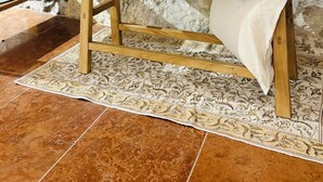 A wooden bench with a vase and bowl in a rustic room with stone walls and patterned floor tiles.