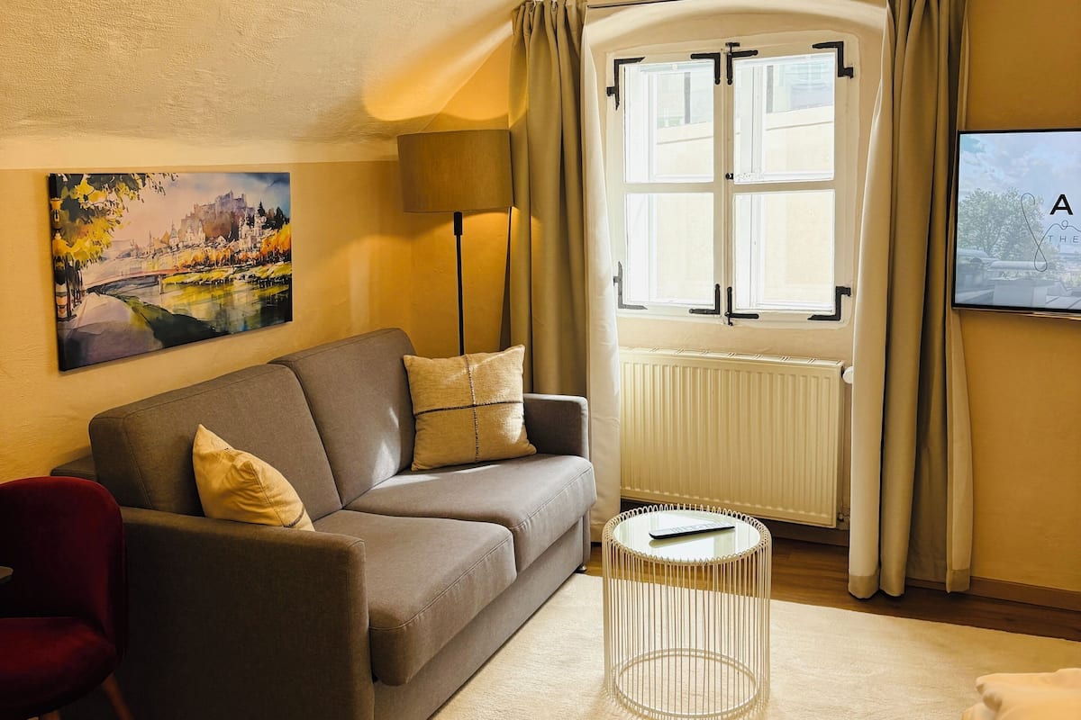A cozy living room with a sofa, a red chair, a round coffee table, and a painting on the wall.