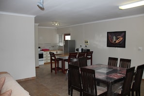 A dining area with a table and chairs, a kitchen in the background, and a framed artwork on the wall. - Anandi Guesthouse Swakopmund (Swakopmund)