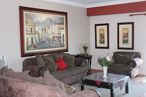 A living room with a sofa, armchairs, a coffee table, and a painting on the wall. - Anandi Guesthouse Swakopmund (Swakopmund)