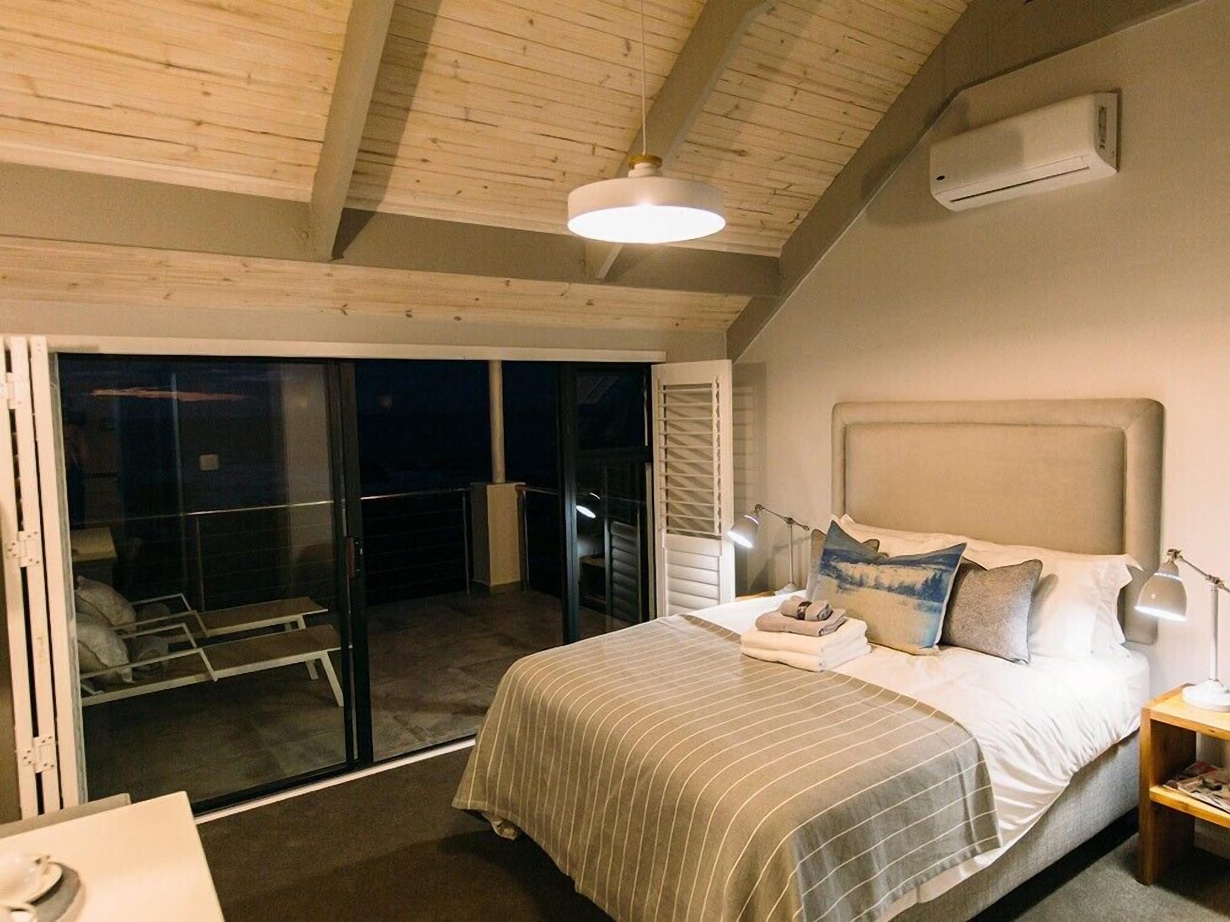 A bedroom with a large bed, a nightstand, a lamp, and a sliding glass door leading to a balcony.