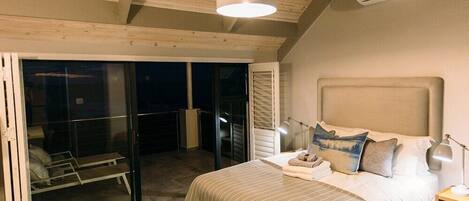 A bedroom with a large bed, a nightstand, a lamp, and a sliding glass door leading to a balcony.