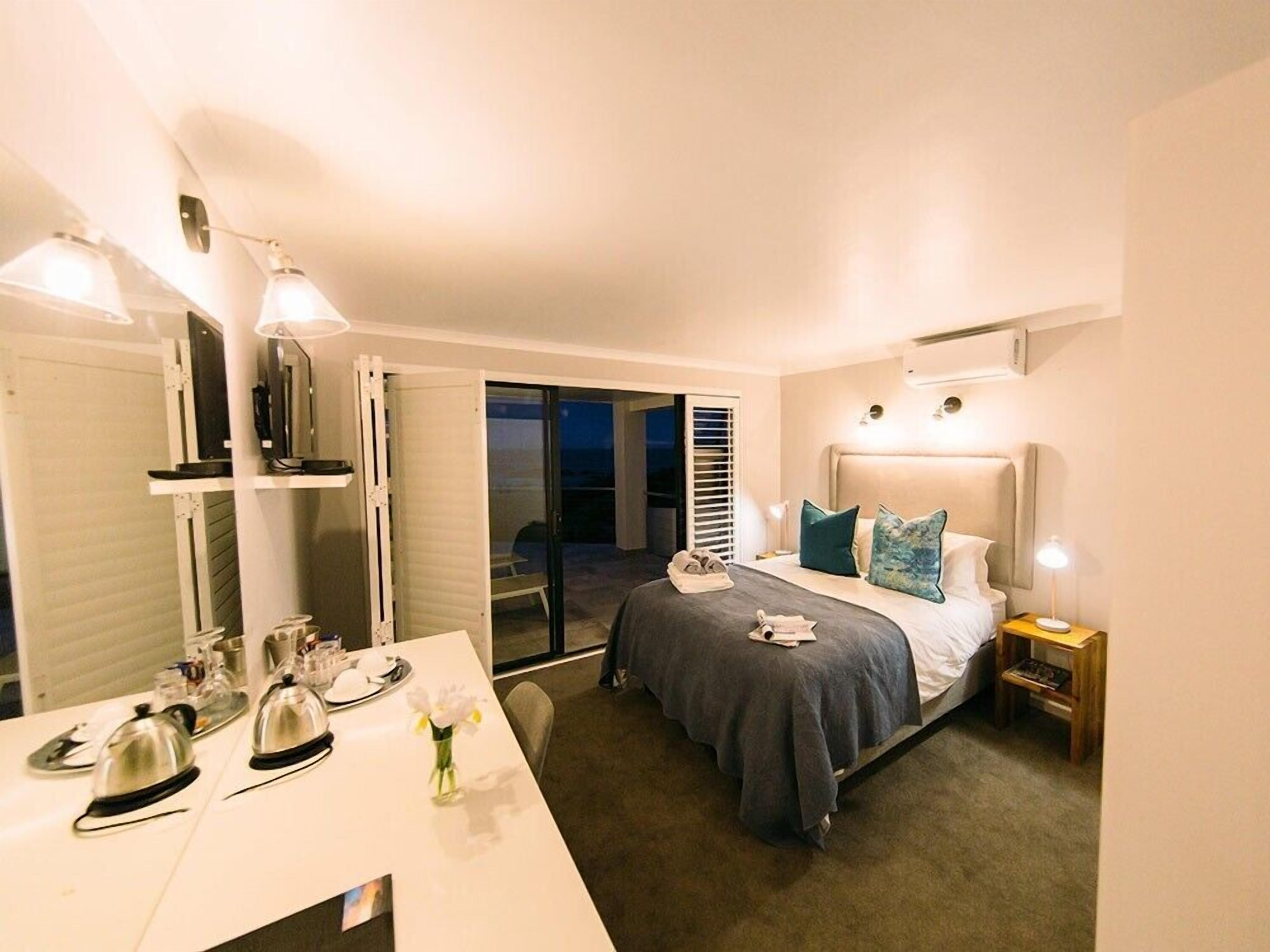 A hotel room with a bed, a desk with a mirror, and a view of the outside.