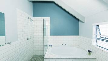 Une salle de bain moderne avec des carreaux blancs, une douche en verre, une baignoire sur pieds et une fenêtre avec des stores.