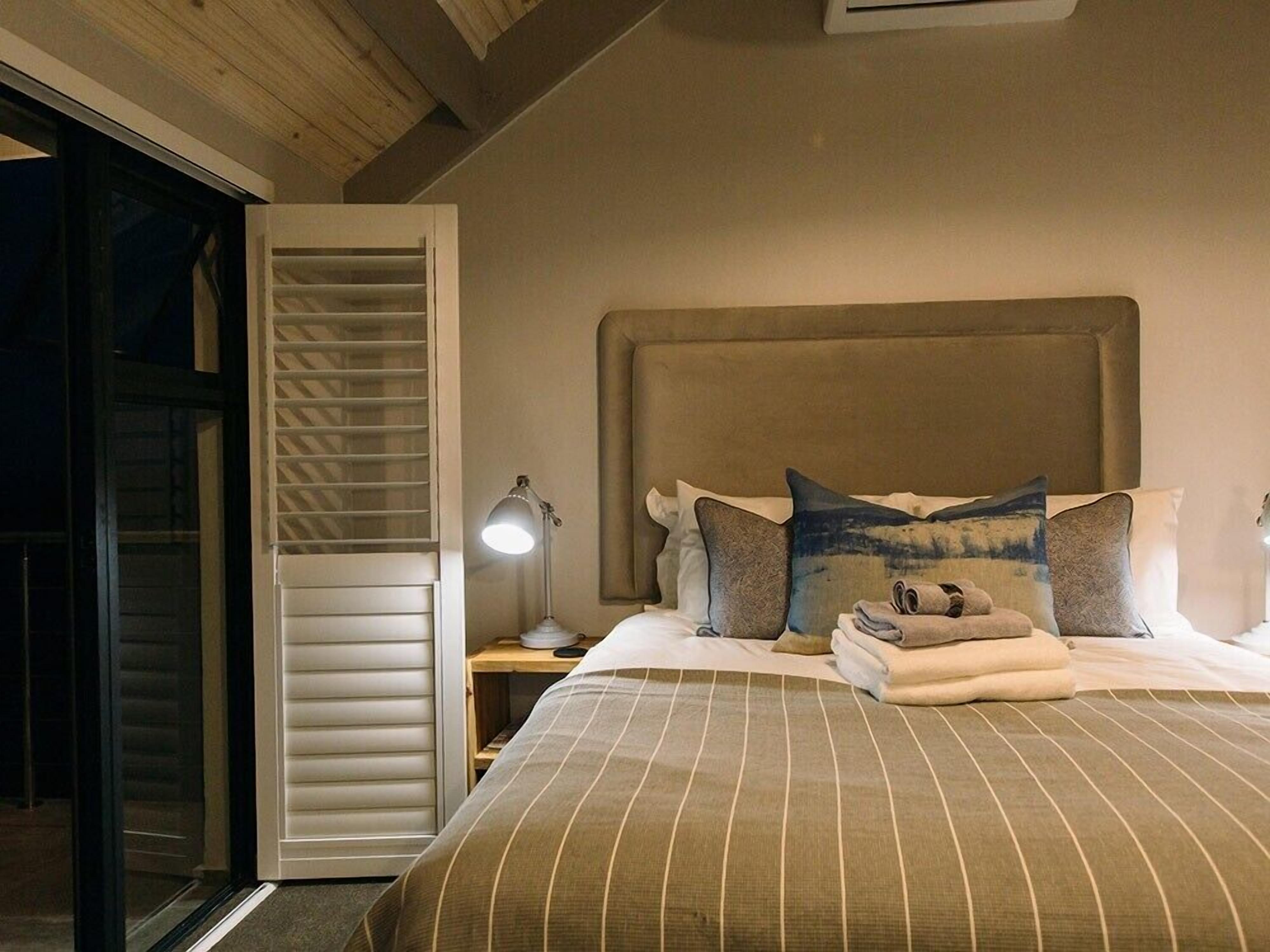A bedroom with a large bed, a nightstand with a lamp, a sliding door, and a headboard.