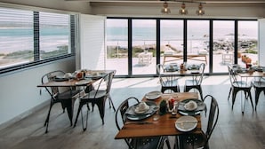 Ein Essbereich mit Tischen für vier Personen, große Fenster mit Blick auf den Strand und ein modernes Interieur.