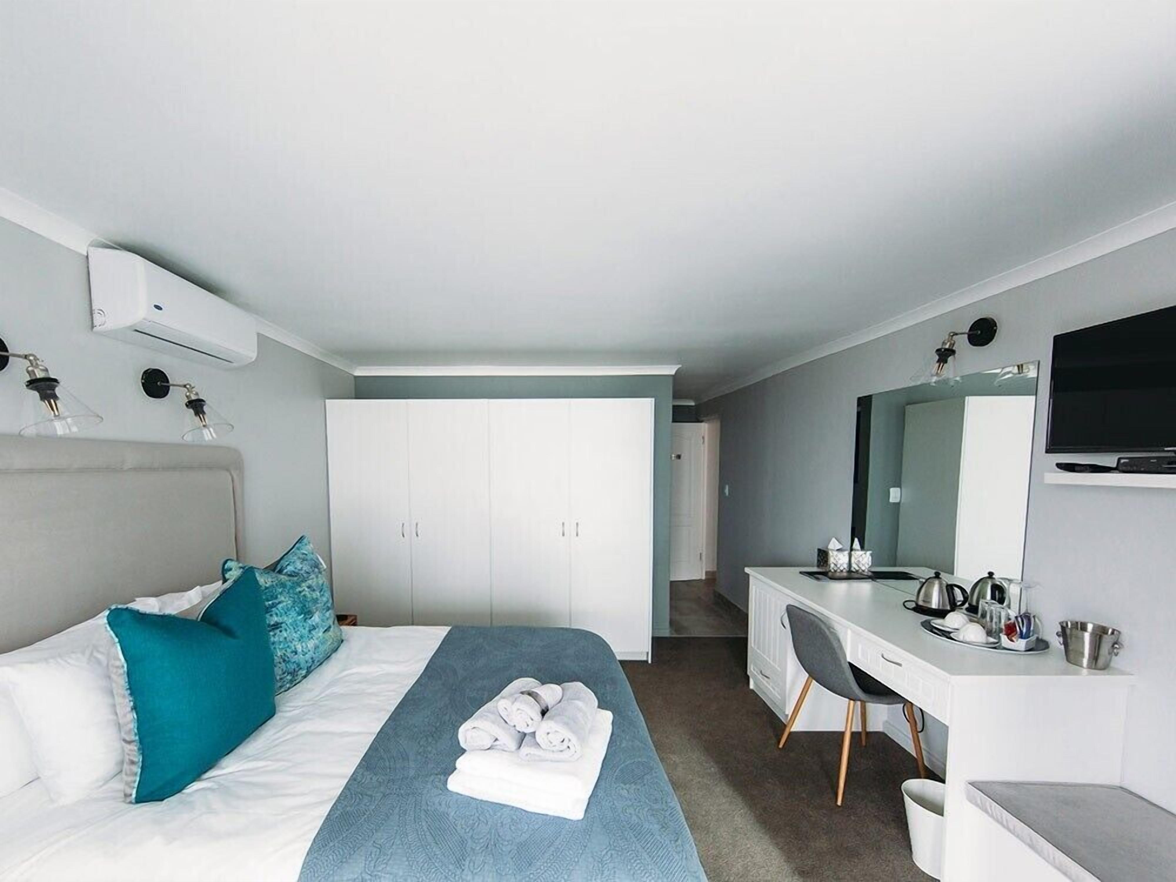 Ett modernt hotellrum med en säng, ett skrivbord, en stol, en TV och en garderob.