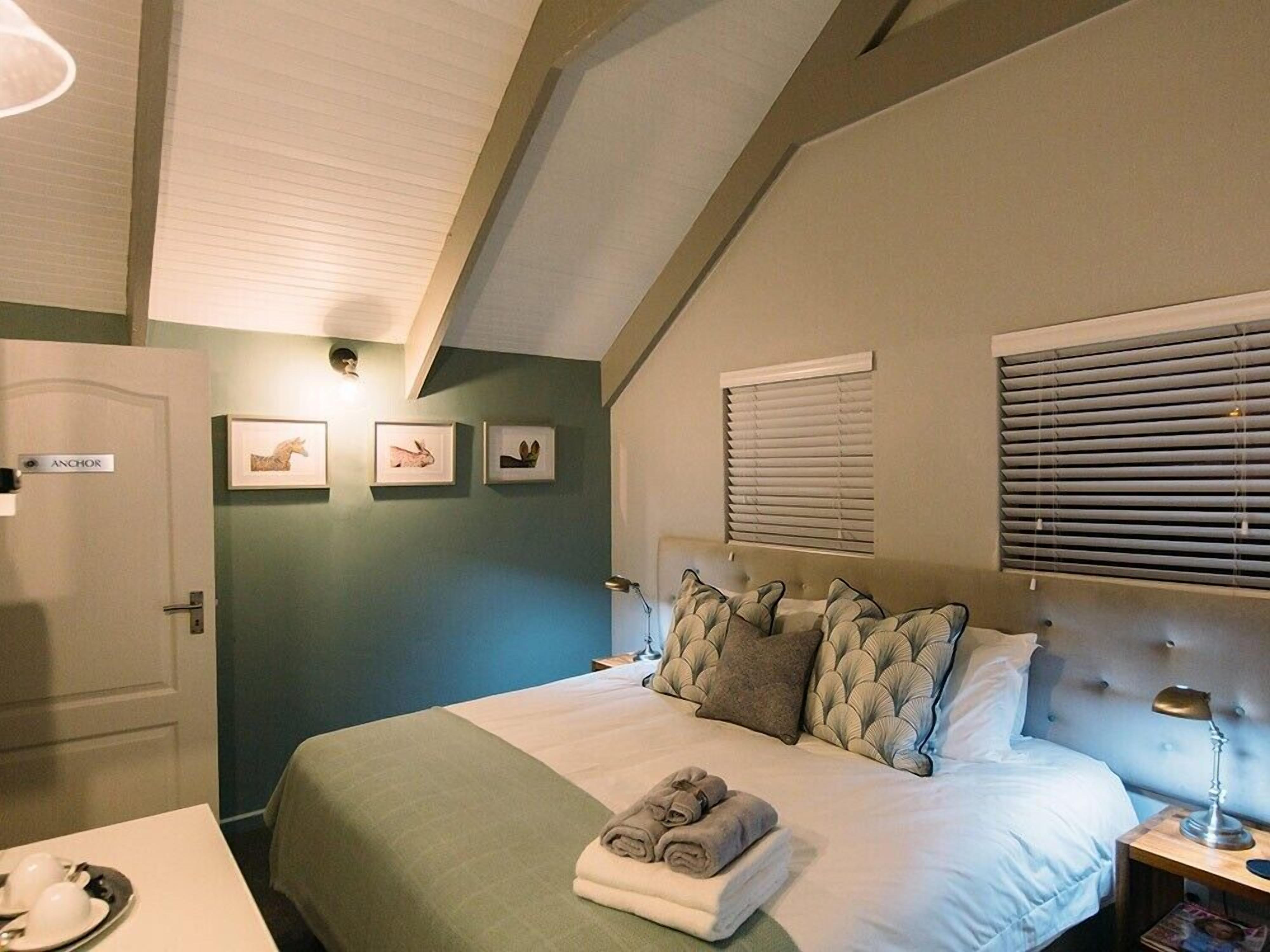Un dormitorio con cama, mesita de noche, puerta con la leyenda 'Anchor' y cuadros enmarcados en la pared.