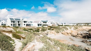 Eine Reihe moderner, weißer Gebäude mit flachen Dächern, gelegen an einem sandigen Strand mit vereinzelter Vegetation.