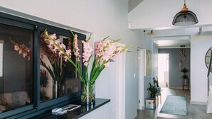 Ein moderner Flur mit einem großen Fenster, einer Vase mit rosa Blumen und einer schwarzen Pendelleuchte.