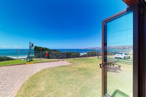 A patio with a view of the sea, a fence, and a car parked nearby.