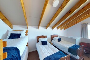 A room with three wooden beds, white bedding, and a wooden ceiling with exposed beams.