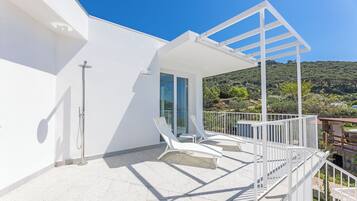 Un balcone moderno con ringhiere bianche, due poltrone da relax e una porta vetrata che dà su un ambiente interno.