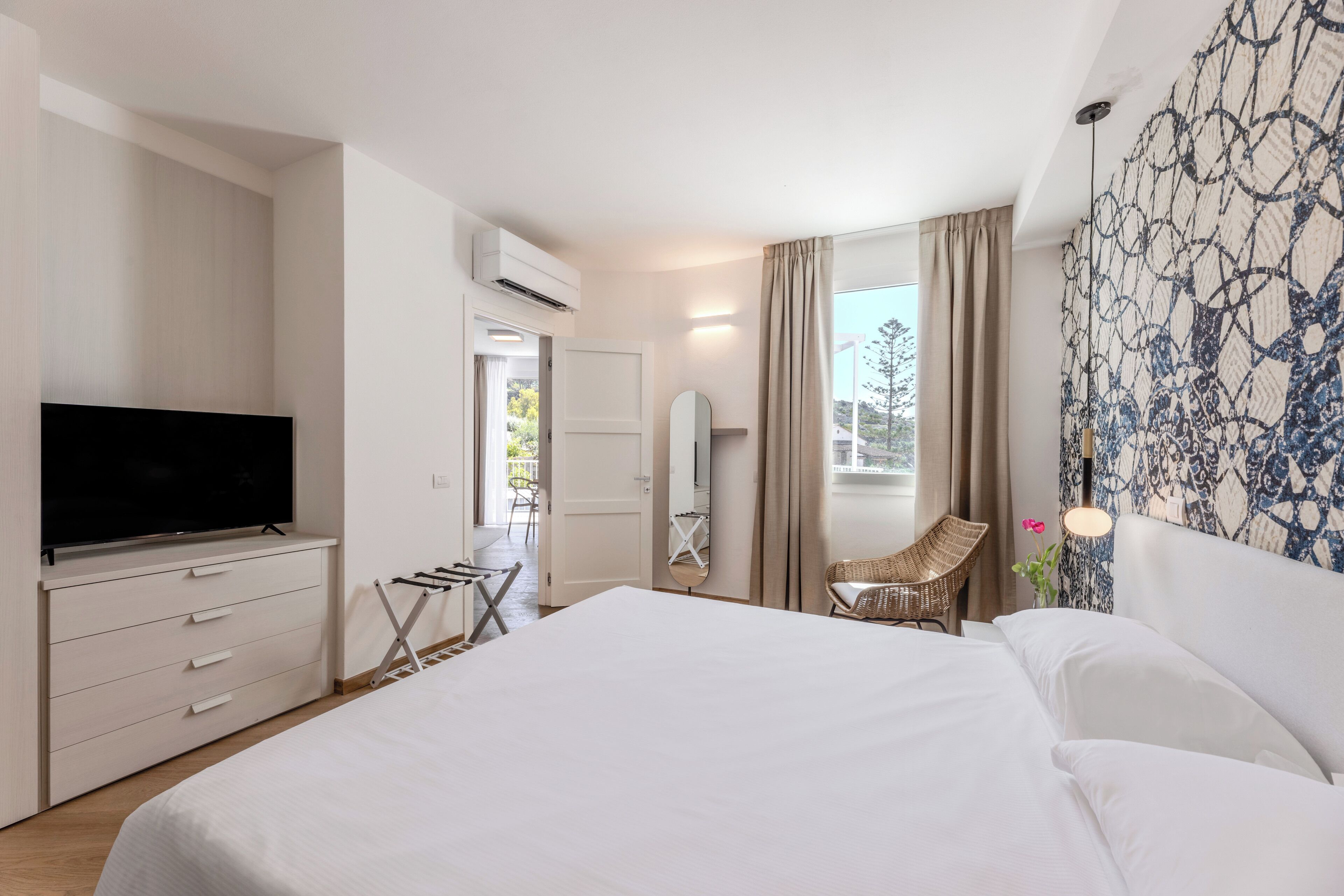 Quarto de hotel moderno com uma cama grande, televisão de tela plana, cômoda, cadeira e janela com cortinas.