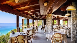 Un restaurant en bord de mer avec une terrasse, des piliers en pierre et des poutres en bois.