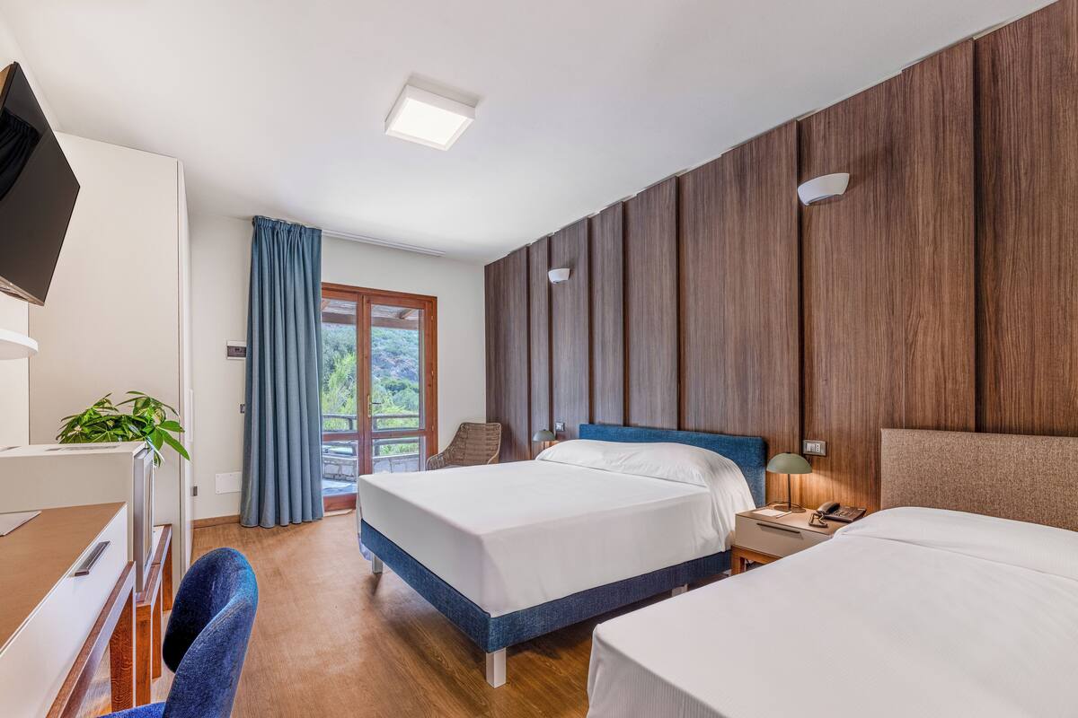 Een hotelkamer met een houten wandpaneel, een bureau met stoel, twee bedden, een televisie en een raam met gordijnen.