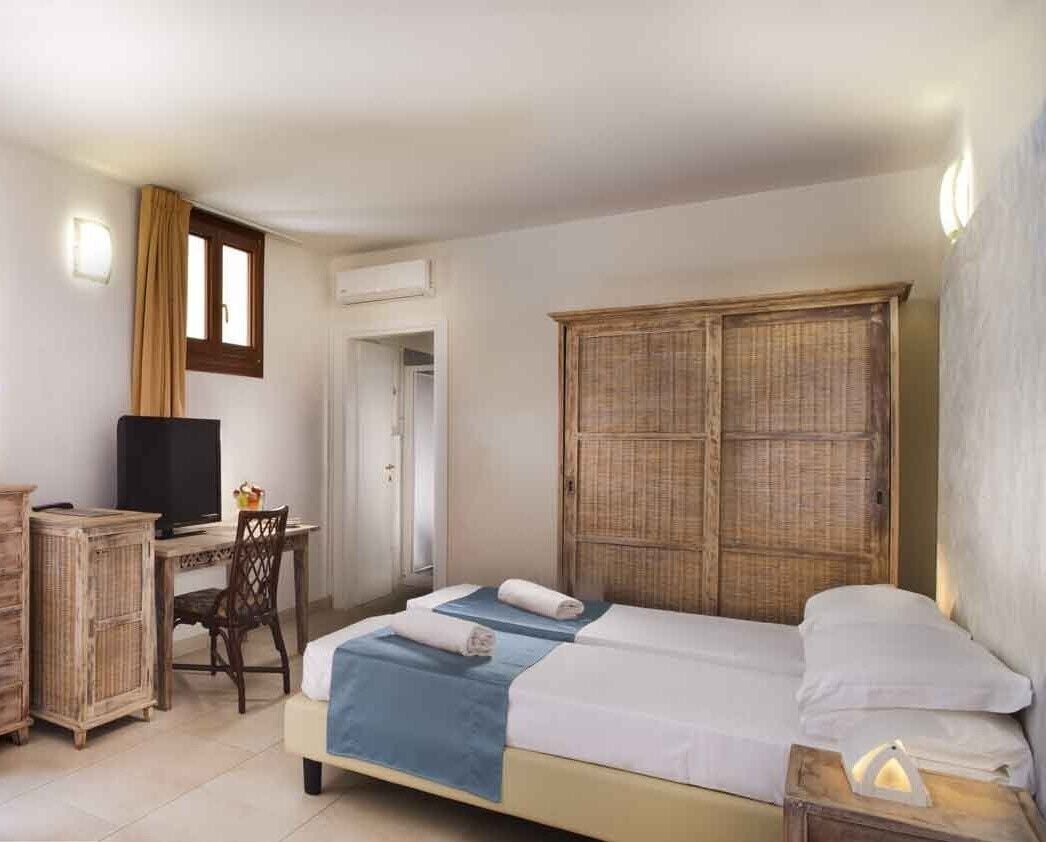 A hotel room with a bed, a desk with a television, a wardrobe, and a chair.