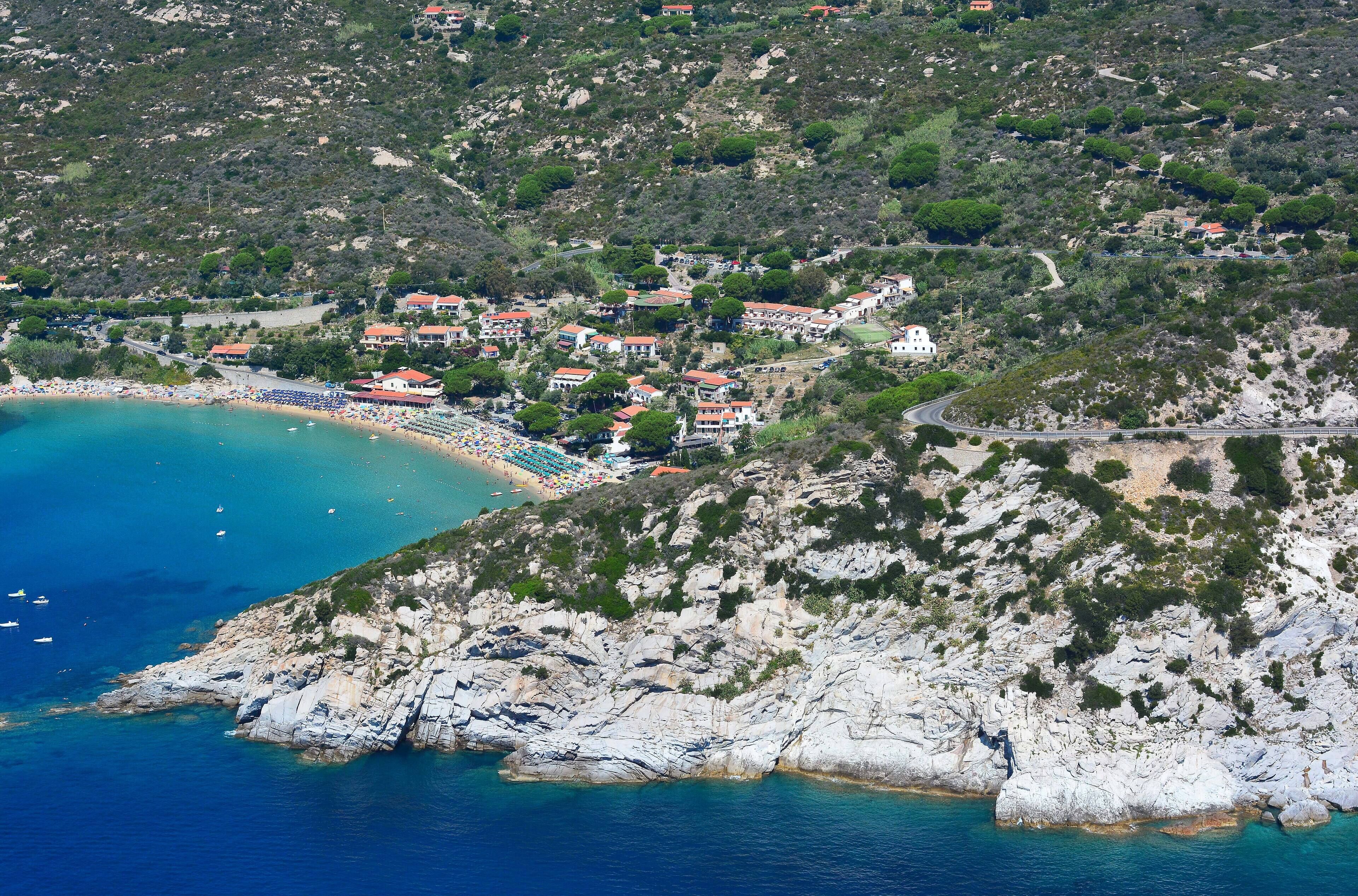 A coastal town with a beach, rocky terrain, and buildings with red roofs.
