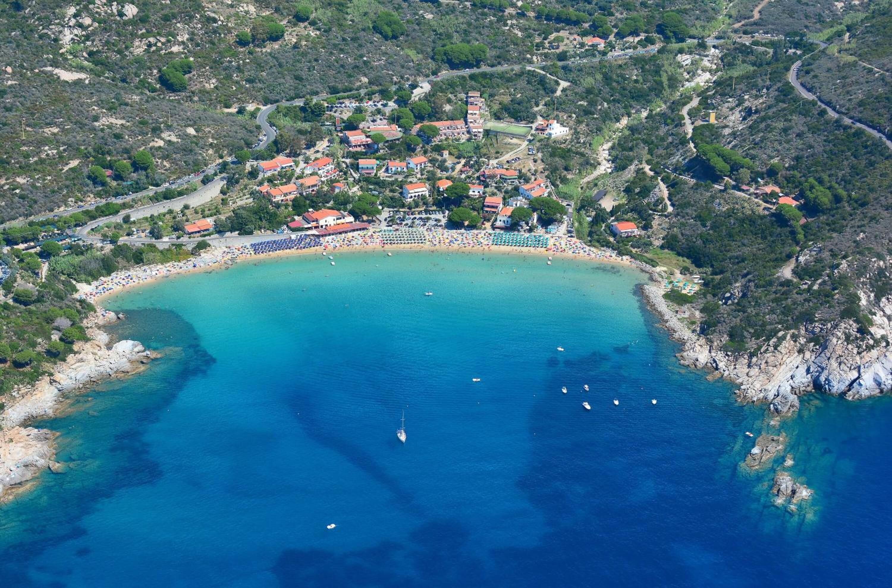 Vista aérea de un pueblo costero con playa, barcos y edificios.