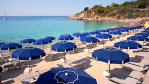 Une plage parsemée de nombreux parasols bleus et de chaises longues.