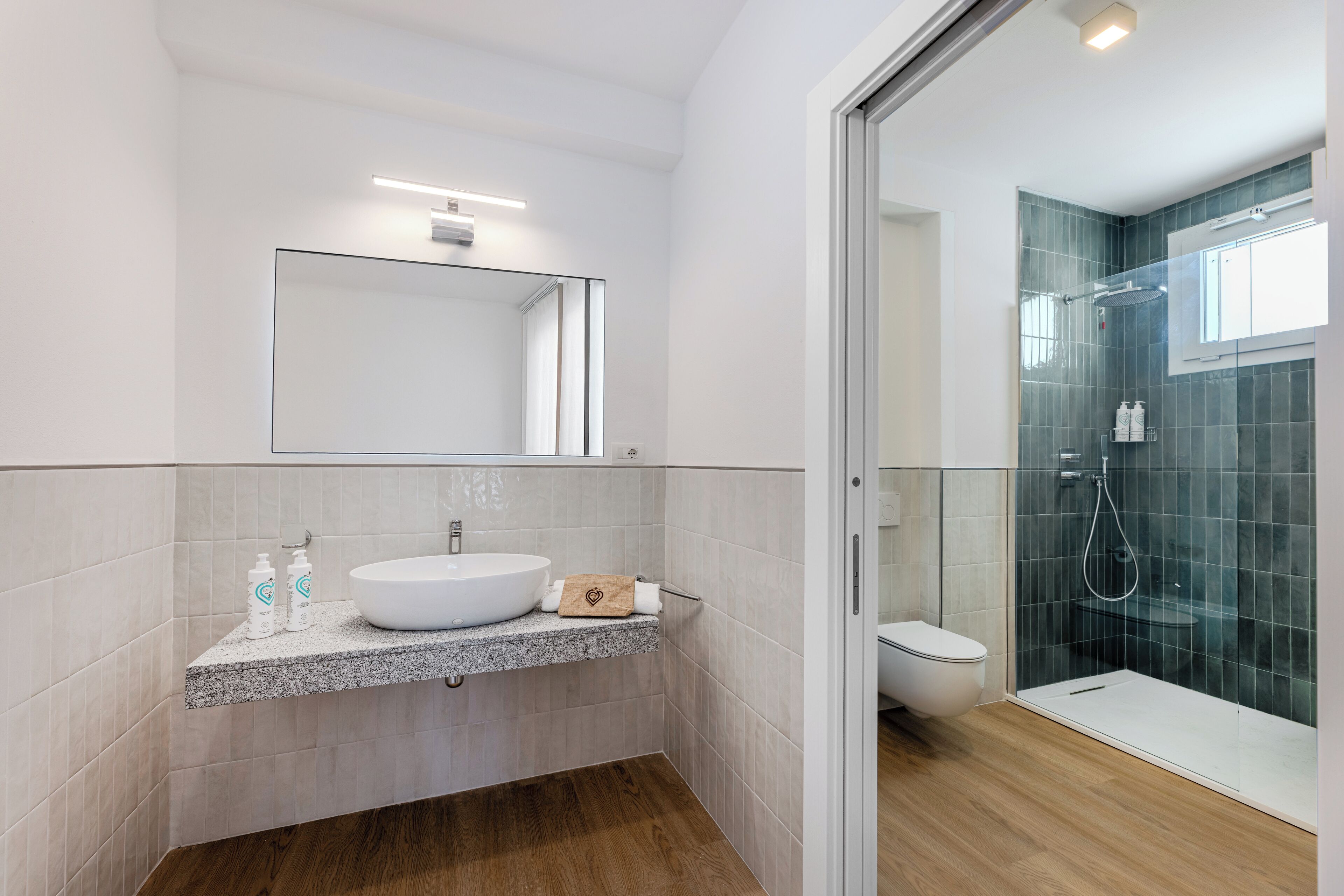 A modern bathroom with a large mirror, a granite countertop, a white sink, and a glass-enclosed shower.