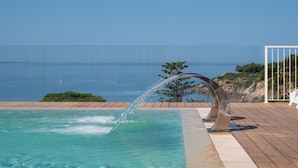 Une piscine agrémentée d’un élément décoratif aquatique, une terrasse en bois et une vue sur la mer.