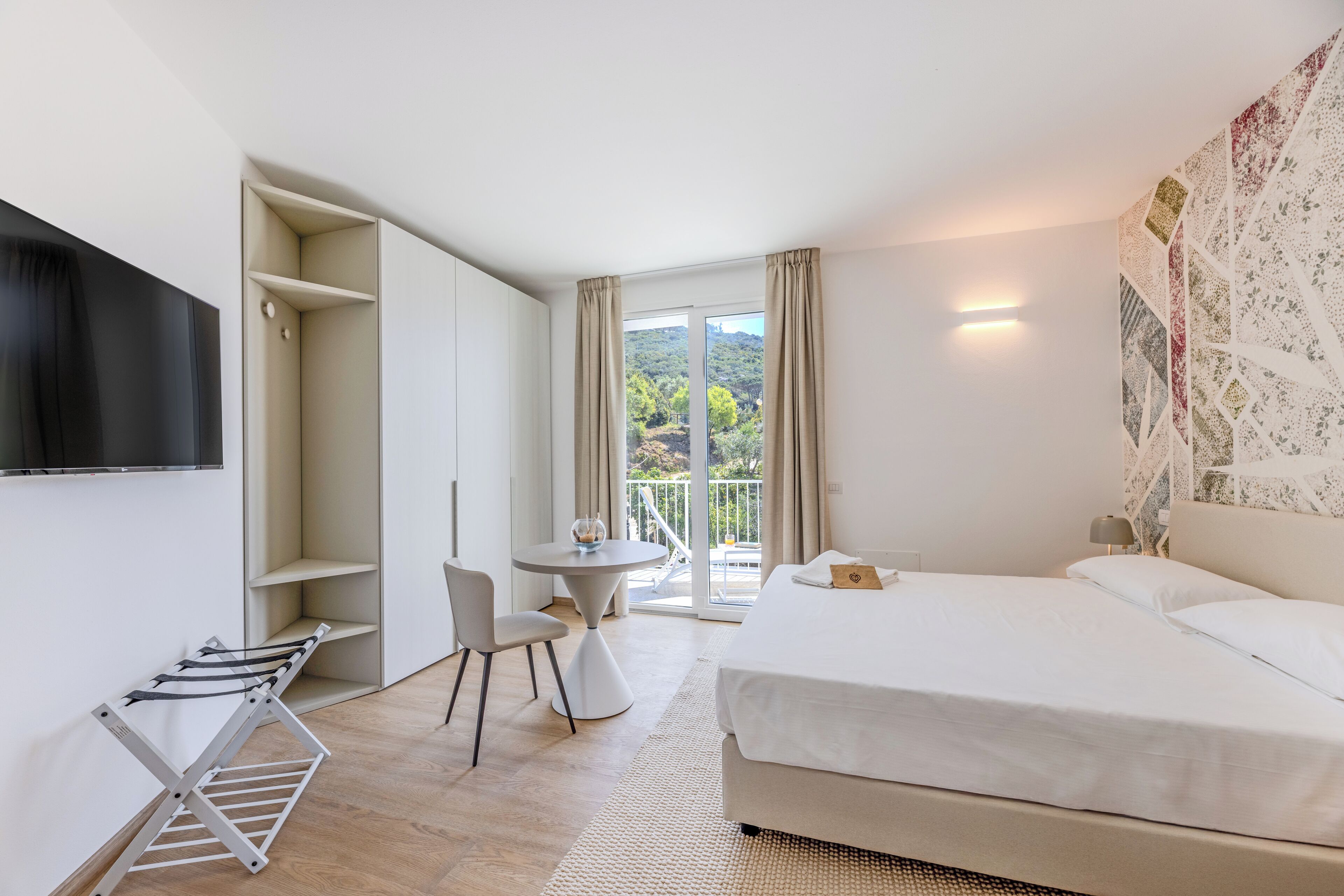 Une chambre d’hôtel moderne, équipée d’un lit, d’un bureau et offrant une vue sur la verdure par la fenêtre.