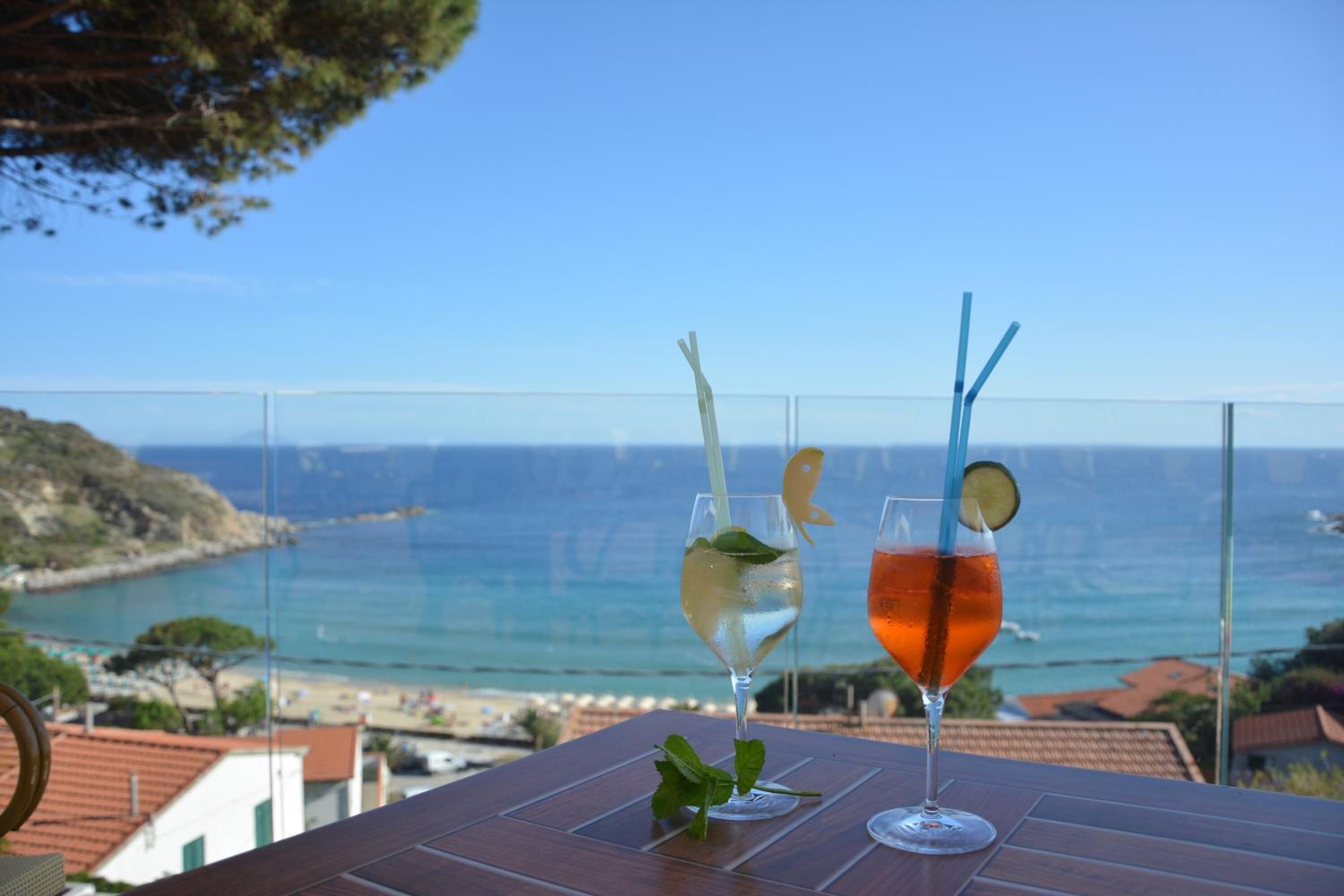 Two glasses of beverages on a table with a view of the sea and coastline.