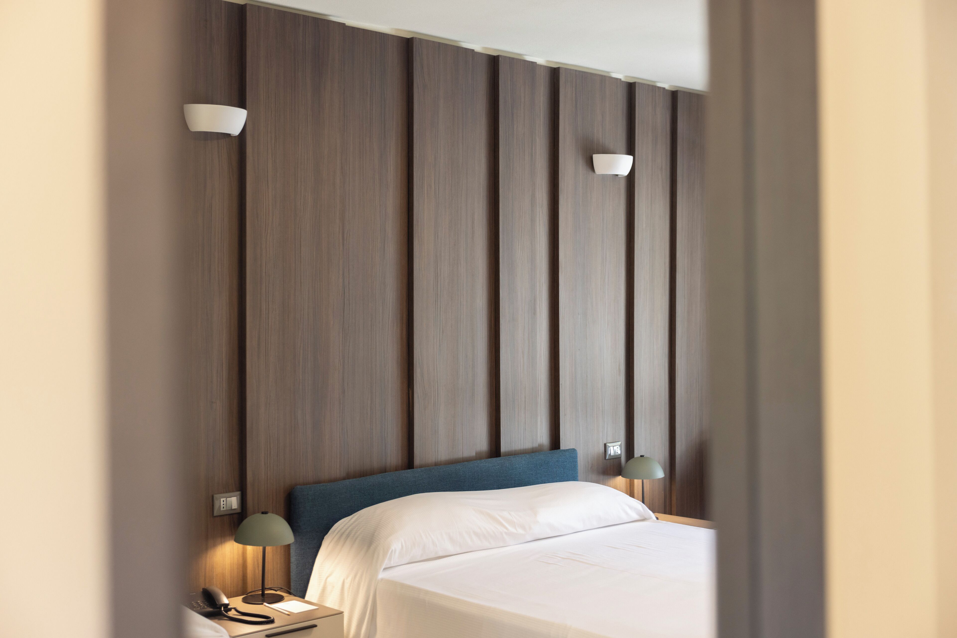 Quarto de hotel com uma cama grande, duas luminárias de cabeceira e painel de parede de madeira.