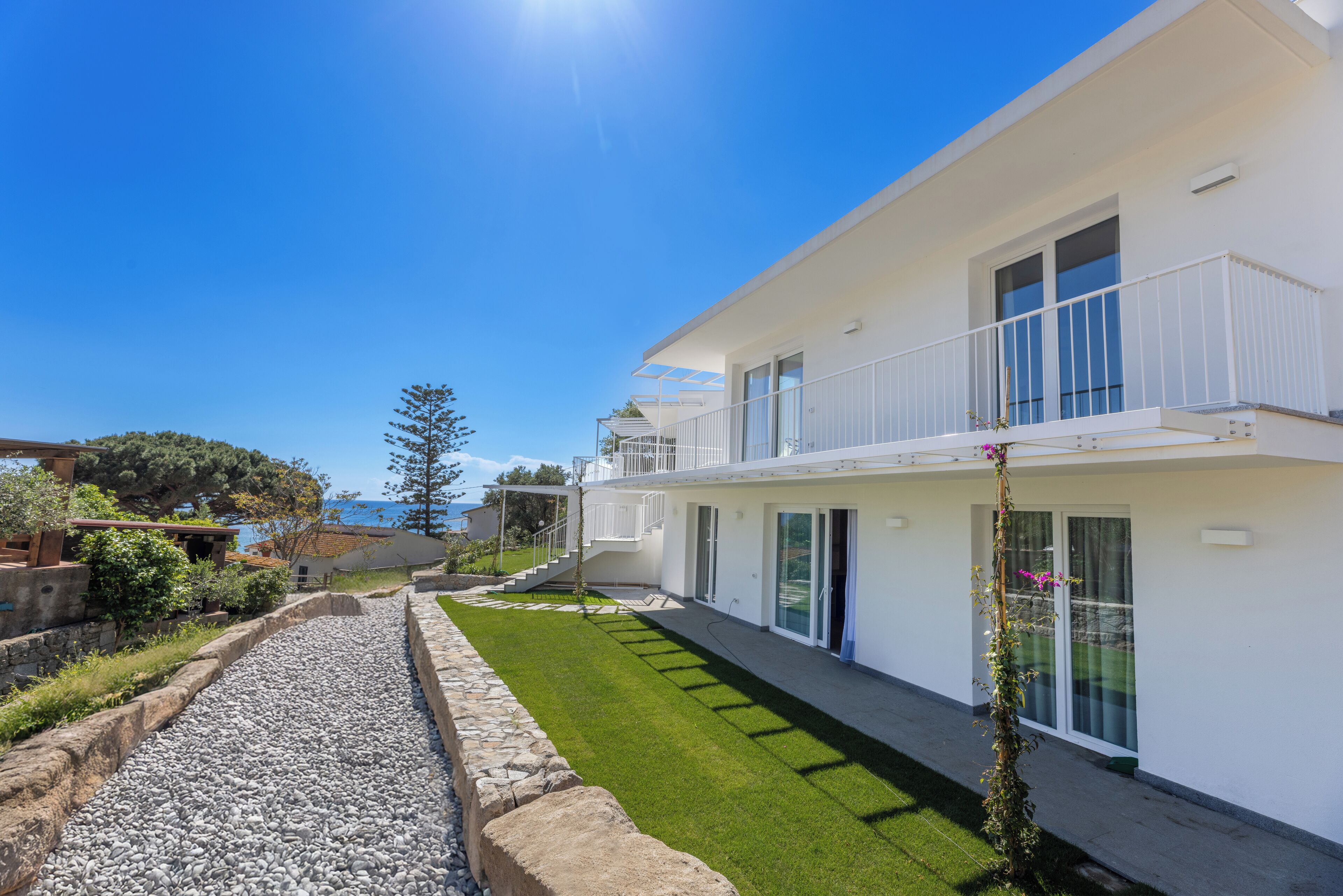 A modern two-story house with a balcony, a well-maintained lawn, and a stone pathway.