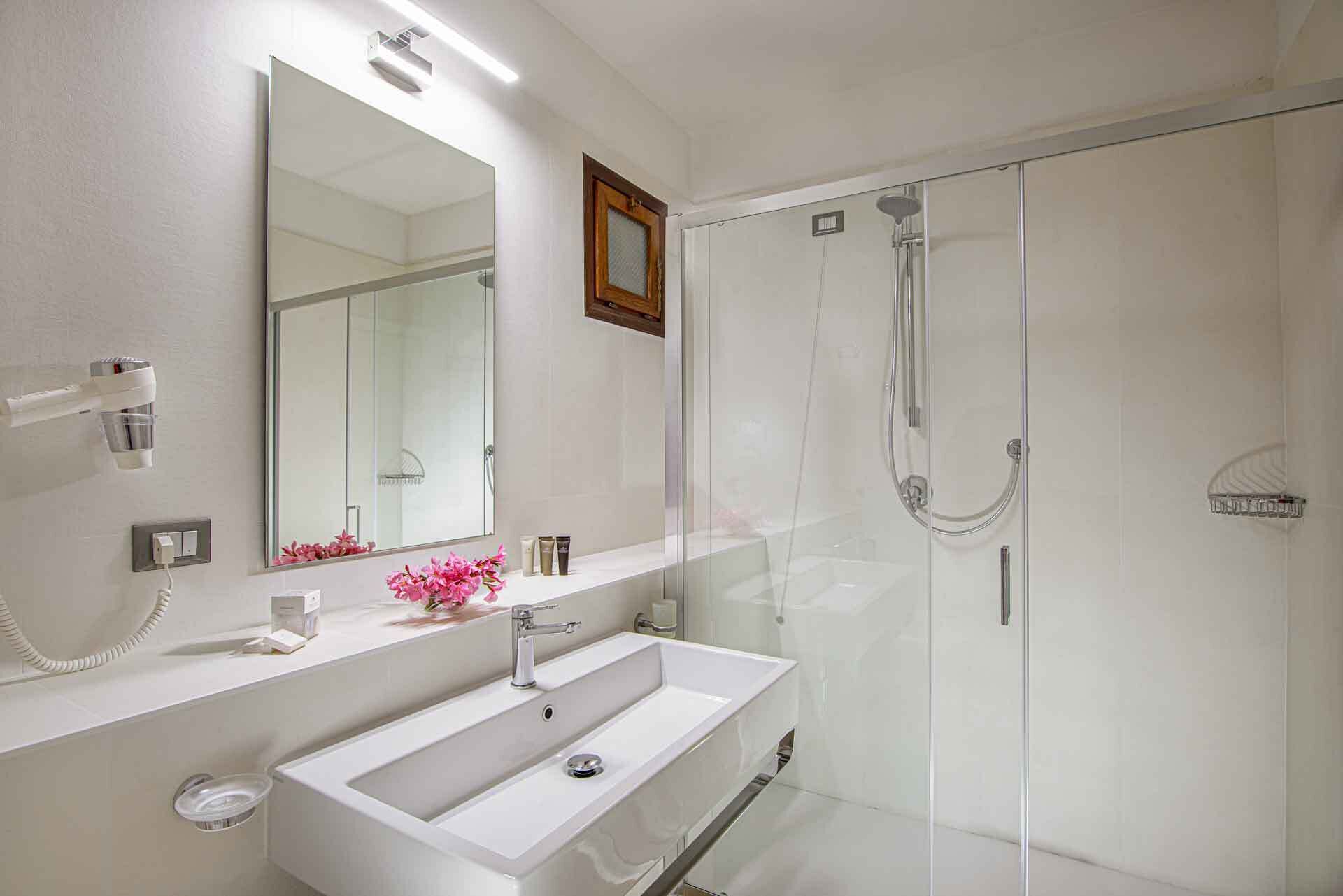 A modern bathroom with a large mirror, a white sink, and a glass-enclosed shower.
