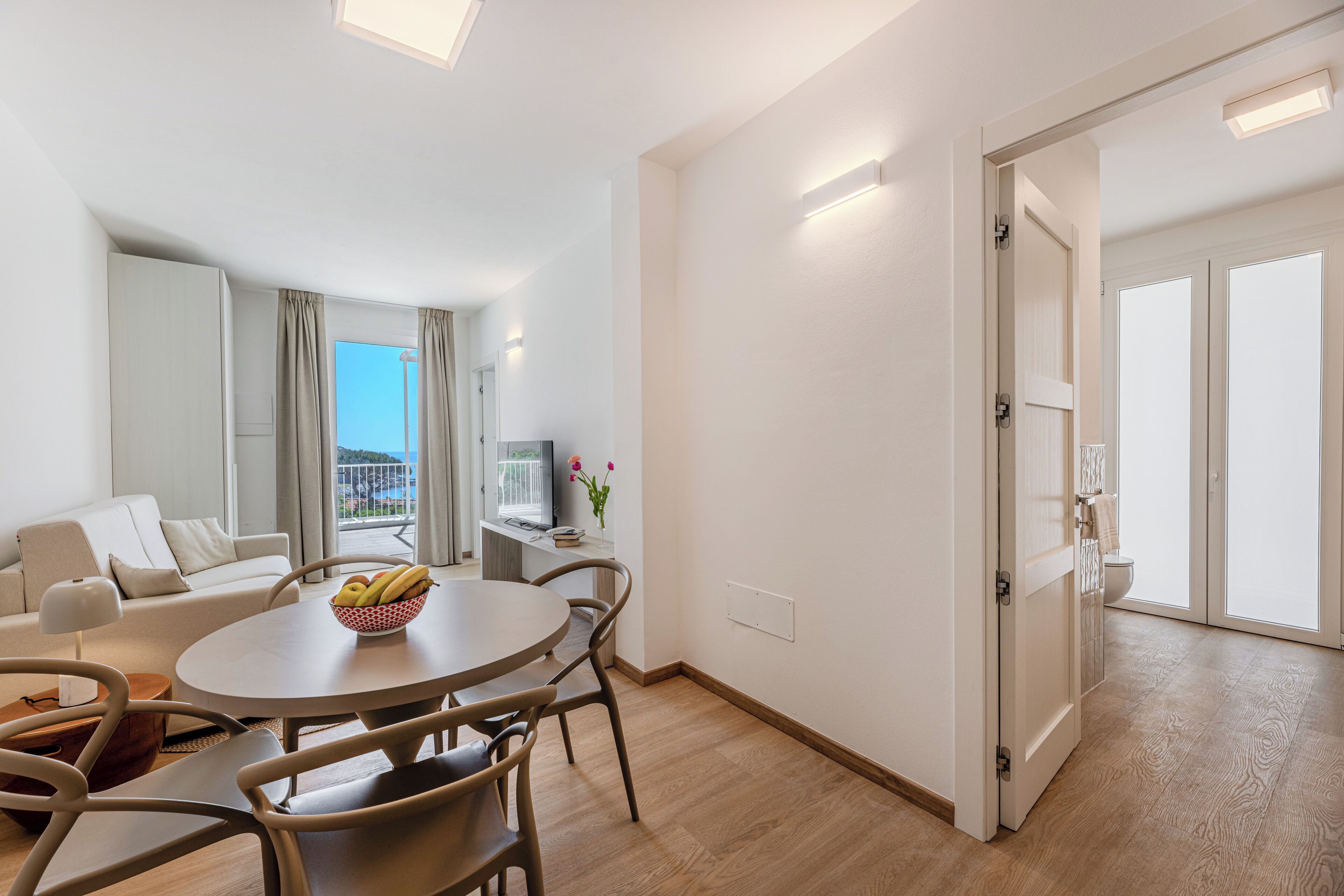 Un salon moderne avec une table à manger ronde, un canapé beige et une vue sur l’extérieur.